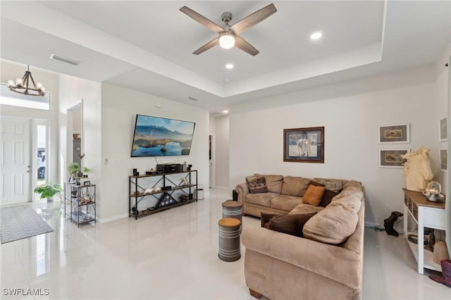 living room featuring a tray ceiling and ceiling fan with notable chandelier