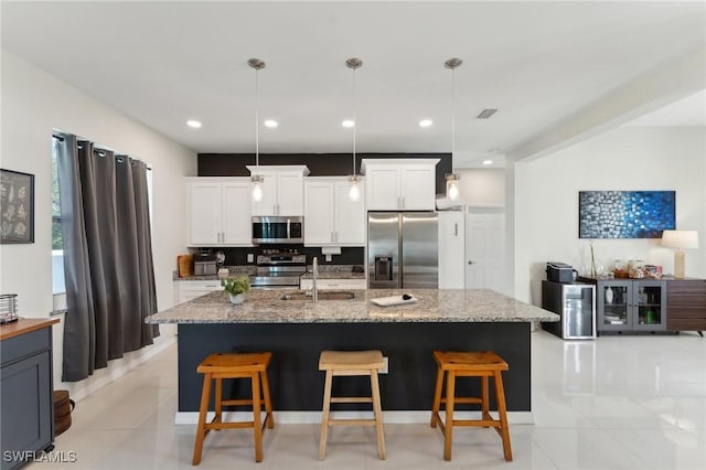 kitchen featuring appliances with stainless steel finishes, sink, a center island with sink, white cabinets, and hanging light fixtures