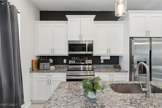 kitchen with light stone countertops, appliances with stainless steel finishes, sink, white cabinetry, and hanging light fixtures