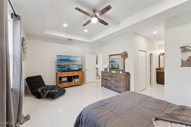 bedroom featuring ceiling fan, ensuite bathroom, and a tray ceiling