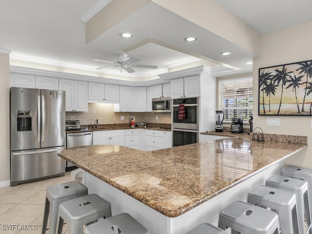 kitchen with ceiling fan, stainless steel appliances, kitchen peninsula, a kitchen bar, and white cabinets