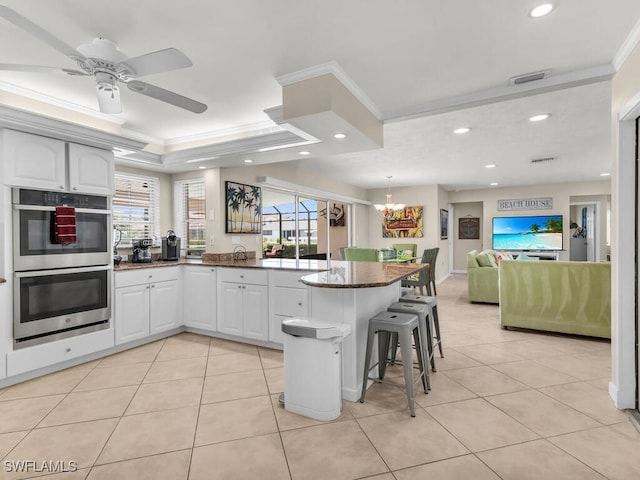 kitchen with white cabinets, a kitchen bar, stainless steel double oven, and a wealth of natural light