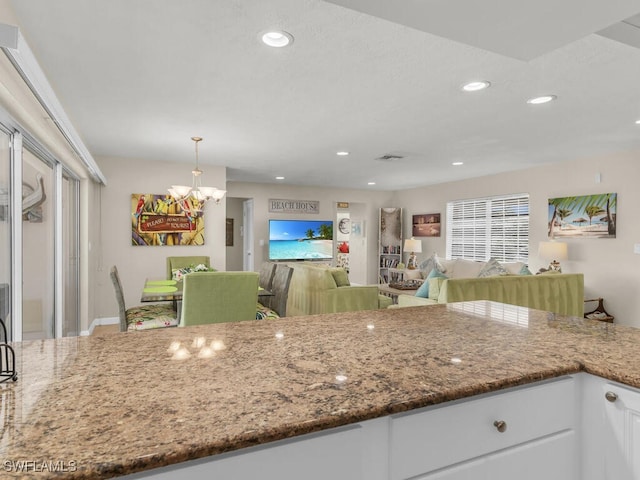 kitchen with white cabinets, a notable chandelier, pendant lighting, and dark stone countertops