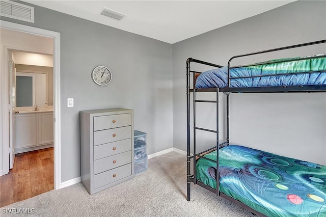 bedroom with connected bathroom, light colored carpet, and sink