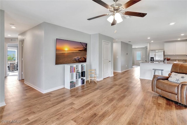 living room with ceiling fan, sink, and light wood-type flooring