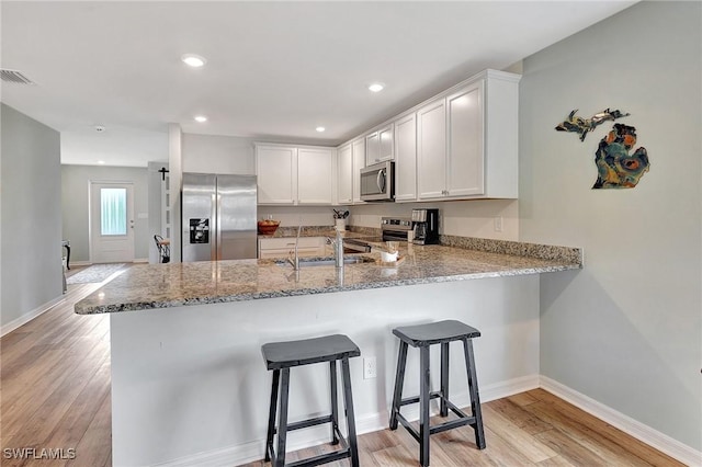 kitchen with kitchen peninsula, stainless steel appliances, white cabinetry, and light hardwood / wood-style flooring