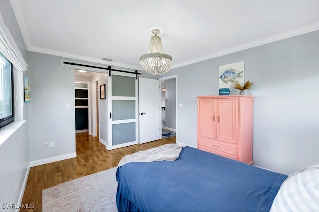 bedroom featuring a barn door, a notable chandelier, crown molding, a walk in closet, and hardwood / wood-style flooring