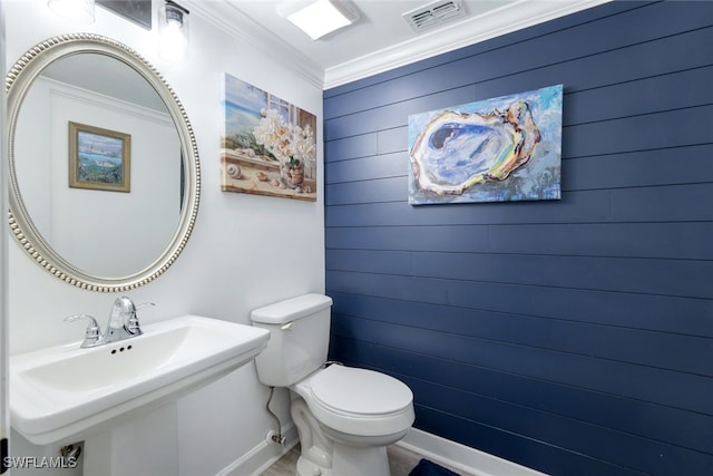 bathroom featuring toilet, ornamental molding, sink, and wooden walls