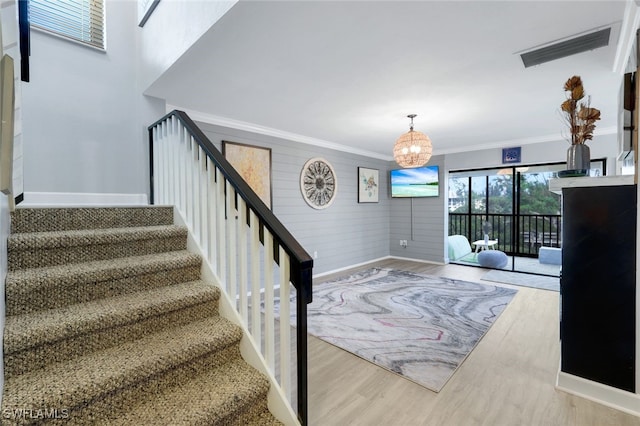 stairs featuring crown molding, wooden walls, a chandelier, and hardwood / wood-style flooring