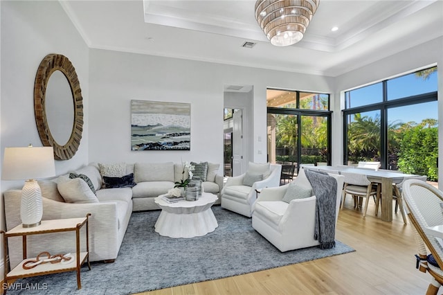 living room with a chandelier, light hardwood / wood-style floors, a tray ceiling, and ornamental molding