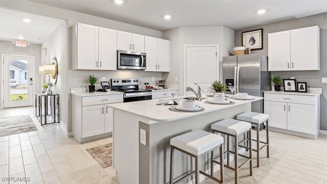 kitchen with an island with sink, white cabinetry, stainless steel appliances, and light countertops