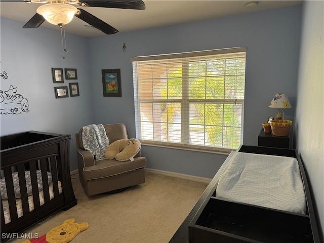 carpeted bedroom with ceiling fan, a crib, and baseboards