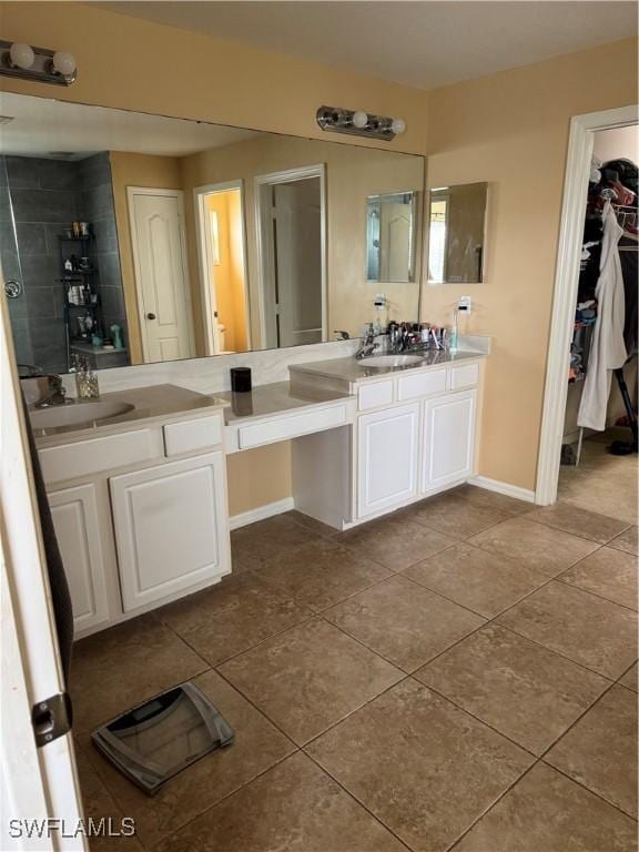 bathroom with vanity, baseboards, a spacious closet, tiled shower, and tile patterned floors