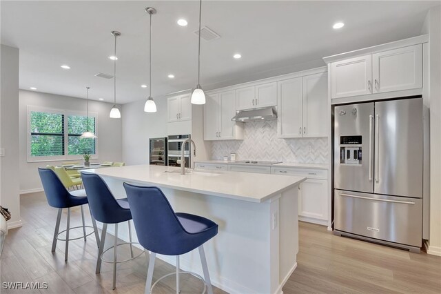 kitchen featuring a kitchen island with sink, sink, hanging light fixtures, white cabinetry, and stainless steel appliances