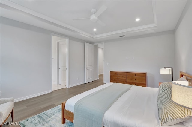 bedroom featuring hardwood / wood-style flooring, ceiling fan, crown molding, and a tray ceiling