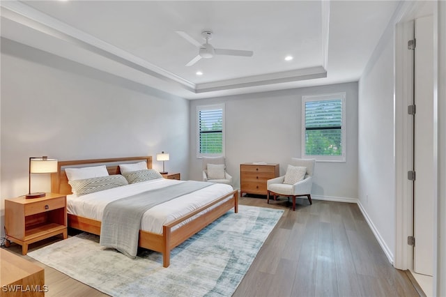 bedroom featuring ceiling fan, light hardwood / wood-style floors, and a tray ceiling