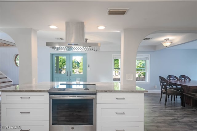 kitchen with stainless steel range with electric cooktop, light stone countertops, a wealth of natural light, island range hood, and white cabinetry