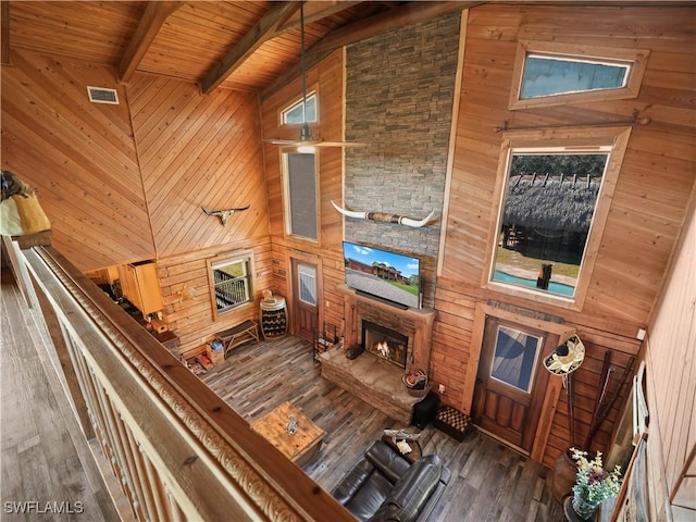 unfurnished living room with wooden ceiling, a stone fireplace, wooden walls, dark hardwood / wood-style floors, and beamed ceiling