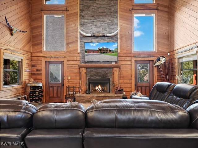 living room featuring a stone fireplace, a towering ceiling, and wooden walls