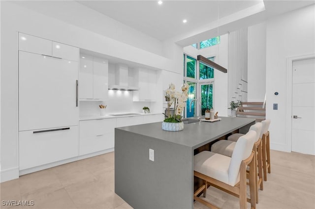 kitchen featuring white cabinetry, wall chimney exhaust hood, a kitchen breakfast bar, electric cooktop, and a kitchen island