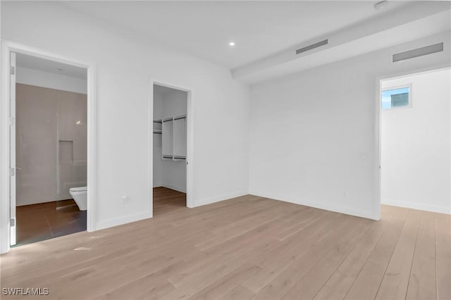 unfurnished bedroom with light wood-type flooring, a closet, a spacious closet, and ensuite bath