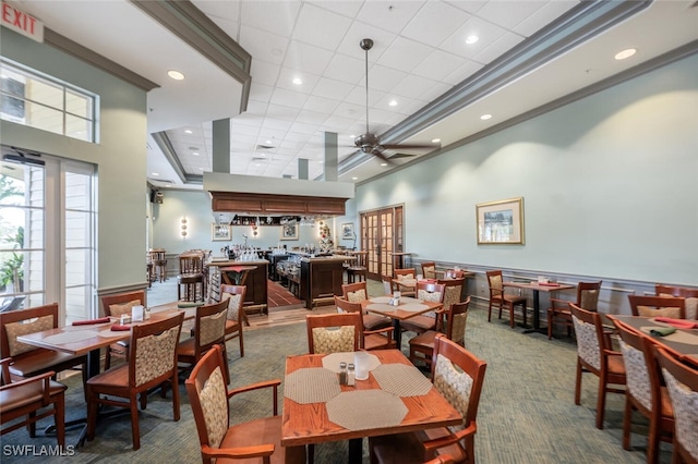 carpeted dining space with a high ceiling, a drop ceiling, crown molding, and ceiling fan