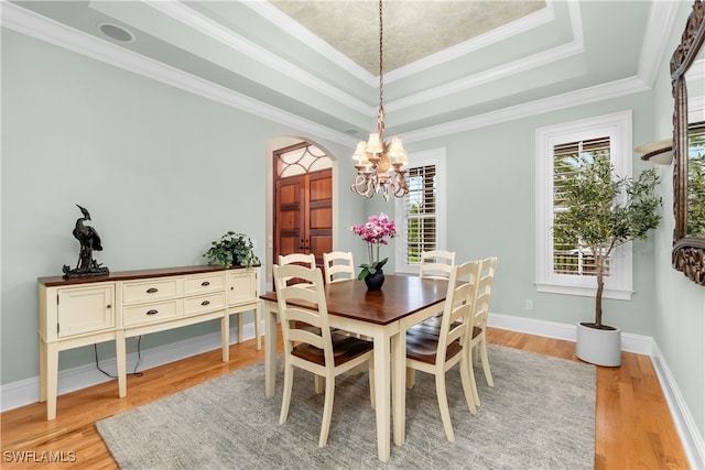 dining area featuring a healthy amount of sunlight, light wood-type flooring, a tray ceiling, and crown molding