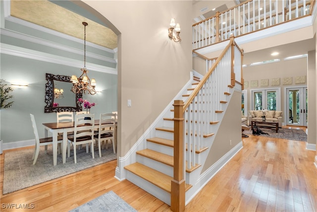 stairs featuring wood-type flooring, a high ceiling, ornamental molding, and a notable chandelier