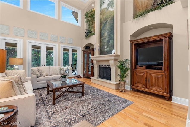 living room featuring wood-type flooring, a towering ceiling, a high end fireplace, and french doors