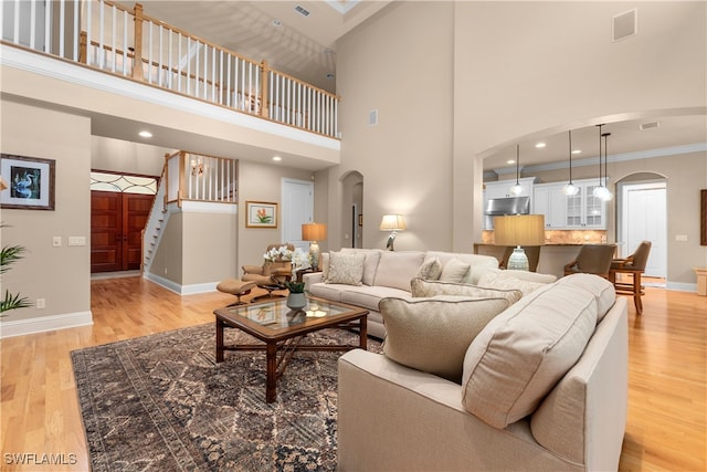 living room with a towering ceiling, light hardwood / wood-style floors, and ornamental molding