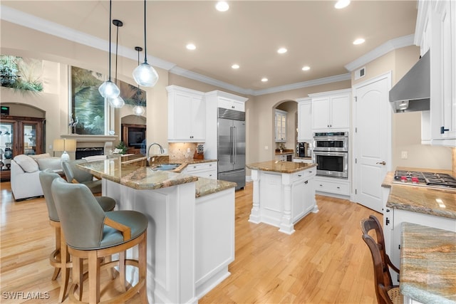 kitchen with sink, wall chimney exhaust hood, stainless steel appliances, backsplash, and decorative light fixtures