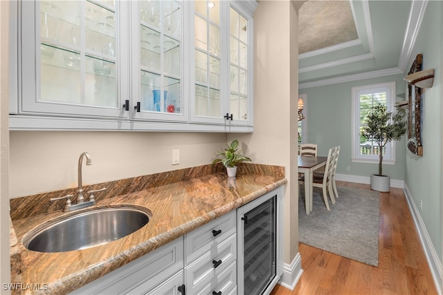 bar with sink, light stone countertops, ornamental molding, white cabinetry, and beverage cooler