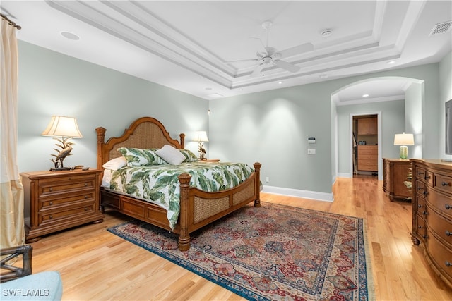 bedroom with ceiling fan, a raised ceiling, crown molding, and light hardwood / wood-style flooring