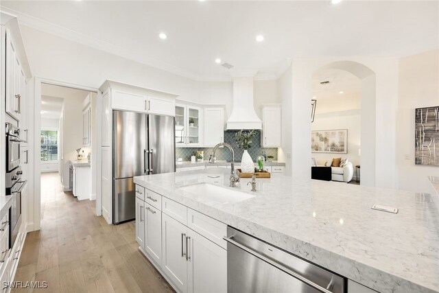 kitchen featuring light stone countertops, white cabinetry, sink, appliances with stainless steel finishes, and custom exhaust hood