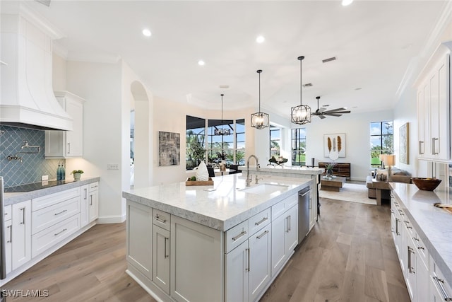 kitchen featuring decorative backsplash, ceiling fan, pendant lighting, a center island with sink, and white cabinetry