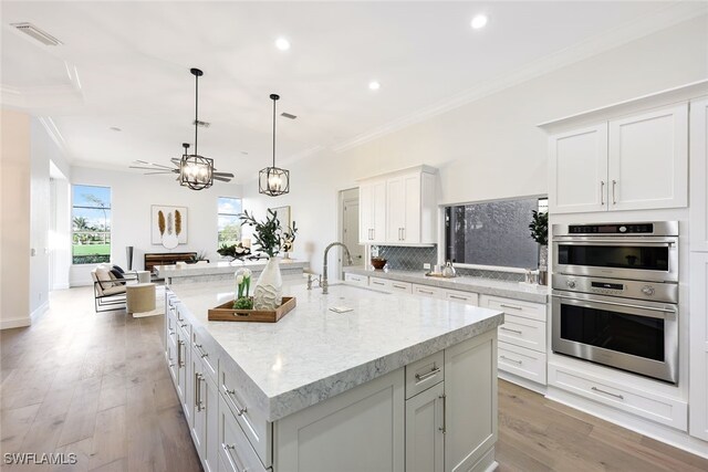 kitchen featuring pendant lighting, double oven, white cabinetry, and a large island with sink