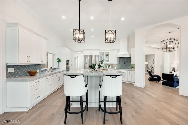 kitchen featuring pendant lighting, custom exhaust hood, stainless steel fridge, and white cabinetry