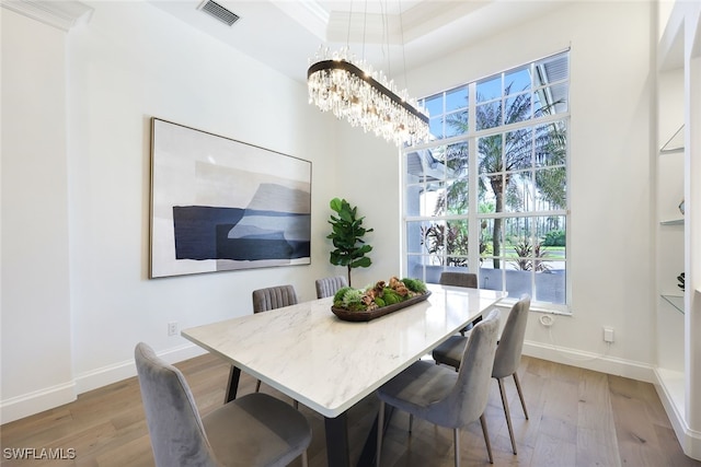 dining area featuring a notable chandelier, light wood-type flooring, crown molding, and a tray ceiling