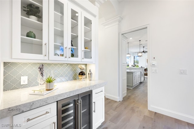 bar featuring white cabinets, light stone counters, light wood-type flooring, and beverage cooler