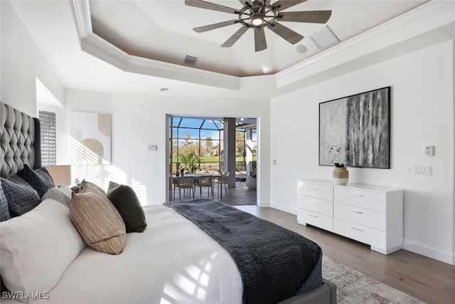 bedroom featuring dark wood-type flooring, ceiling fan, access to exterior, ornamental molding, and a tray ceiling