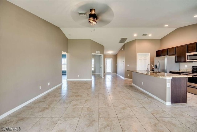 kitchen with ceiling fan, sink, light stone counters, a center island with sink, and appliances with stainless steel finishes