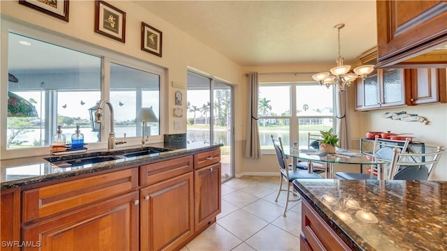 kitchen featuring pendant lighting, sink, dark stone countertops, a chandelier, and light tile patterned floors