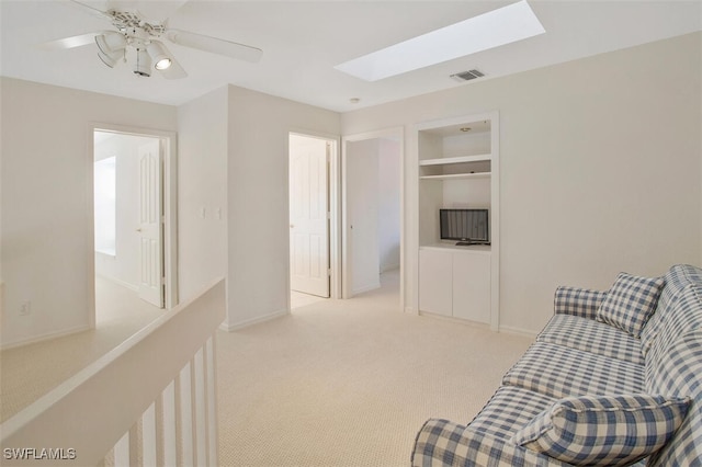 living area with built in shelves, a skylight, light colored carpet, and ceiling fan