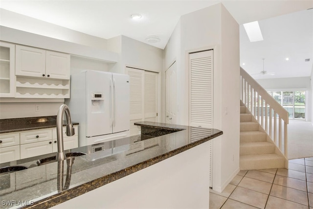 kitchen with sink, white cabinets, dark stone counters, white fridge with ice dispenser, and light tile patterned floors