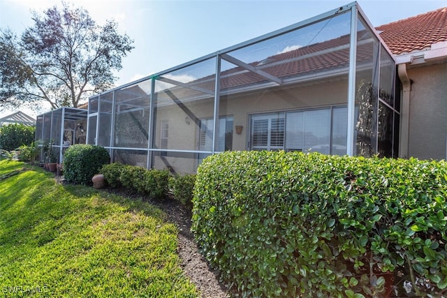 view of side of property featuring glass enclosure and a lawn