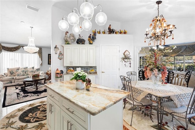 kitchen featuring backsplash, light stone counters, a center island, and an inviting chandelier