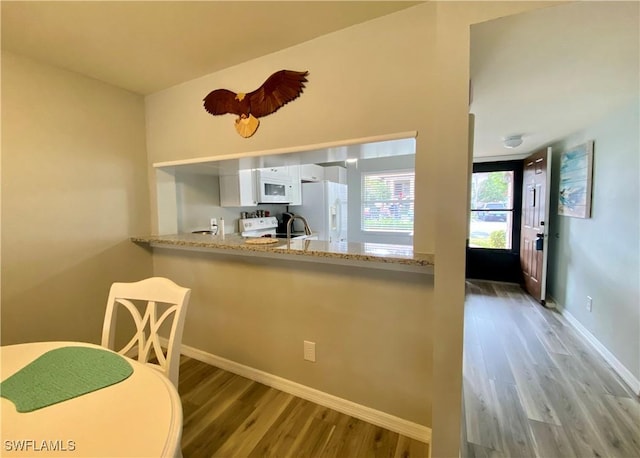 kitchen with wood-type flooring, white cabinets, light stone counters, kitchen peninsula, and white appliances