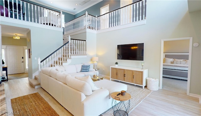 living room featuring light wood-type flooring, a towering ceiling, and crown molding