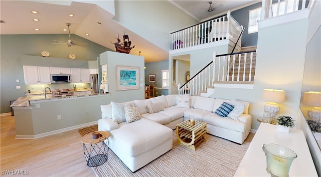 living room with crown molding, sink, ceiling fan, a towering ceiling, and light hardwood / wood-style floors