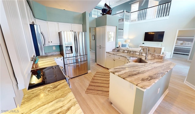 kitchen featuring sink, light stone counters, stainless steel refrigerator with ice dispenser, stainless steel fridge, and a towering ceiling